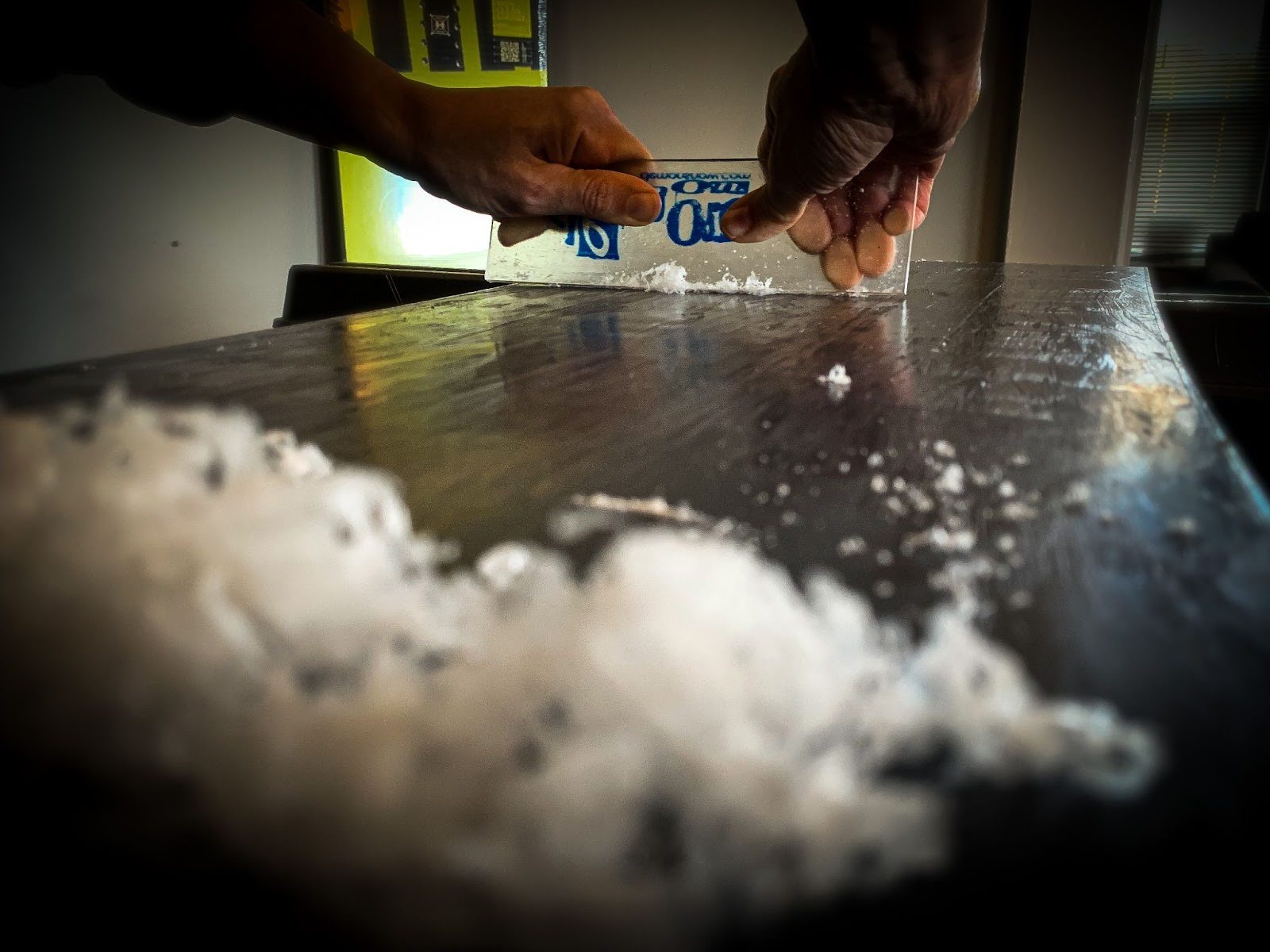 Using a plastic scraper to scrape the excess wax off the base of a snowboard.