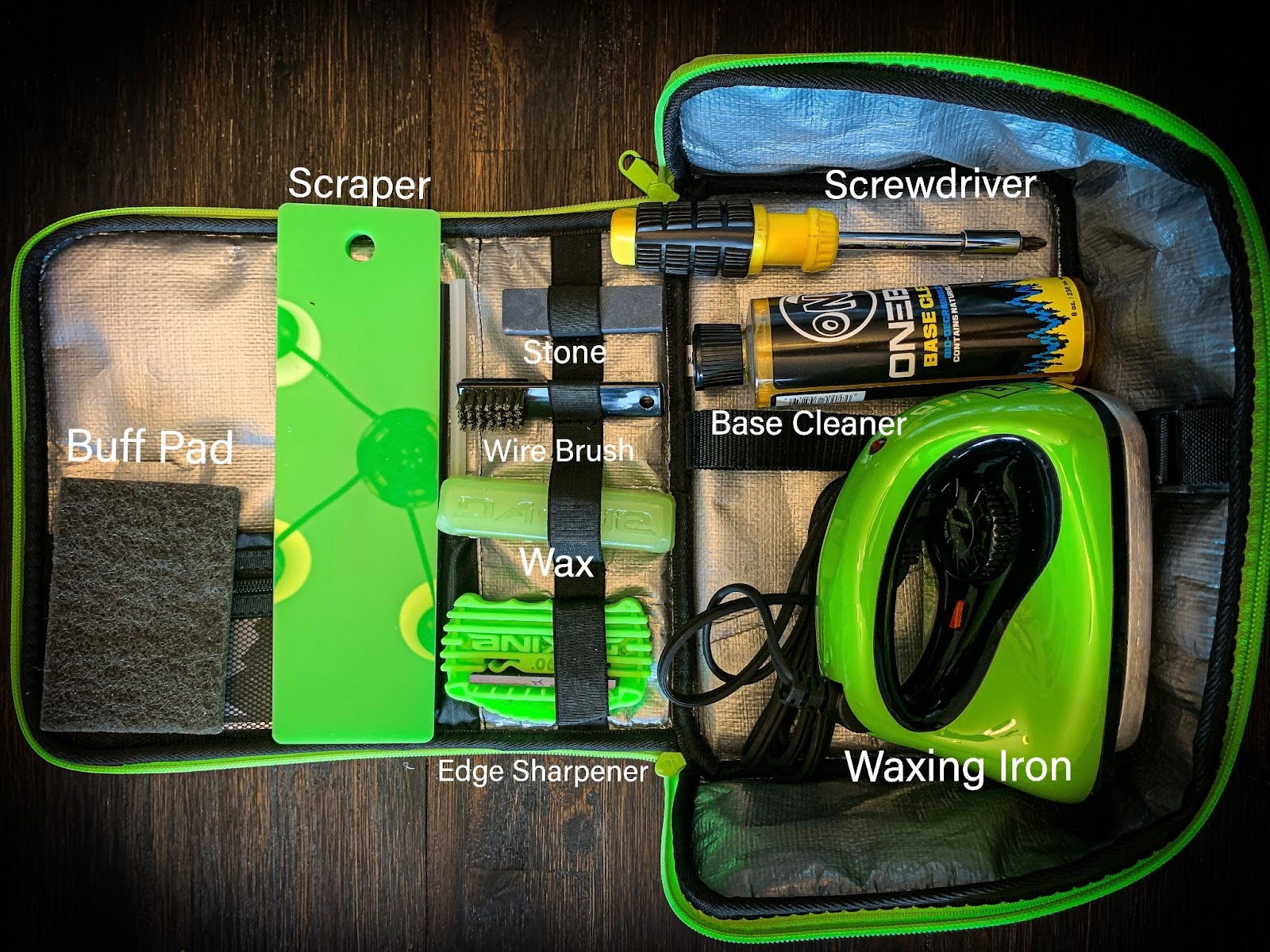 Ski tuning kit with labels that includes a waxing iron, edge sharpener, wax scraper, snowboard wax, buff pad, base cleaner, and screwdriver