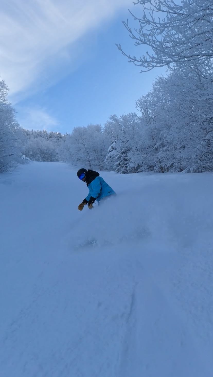Snowboarder in a blue jacket spraying powder at Jay Peak Vermont