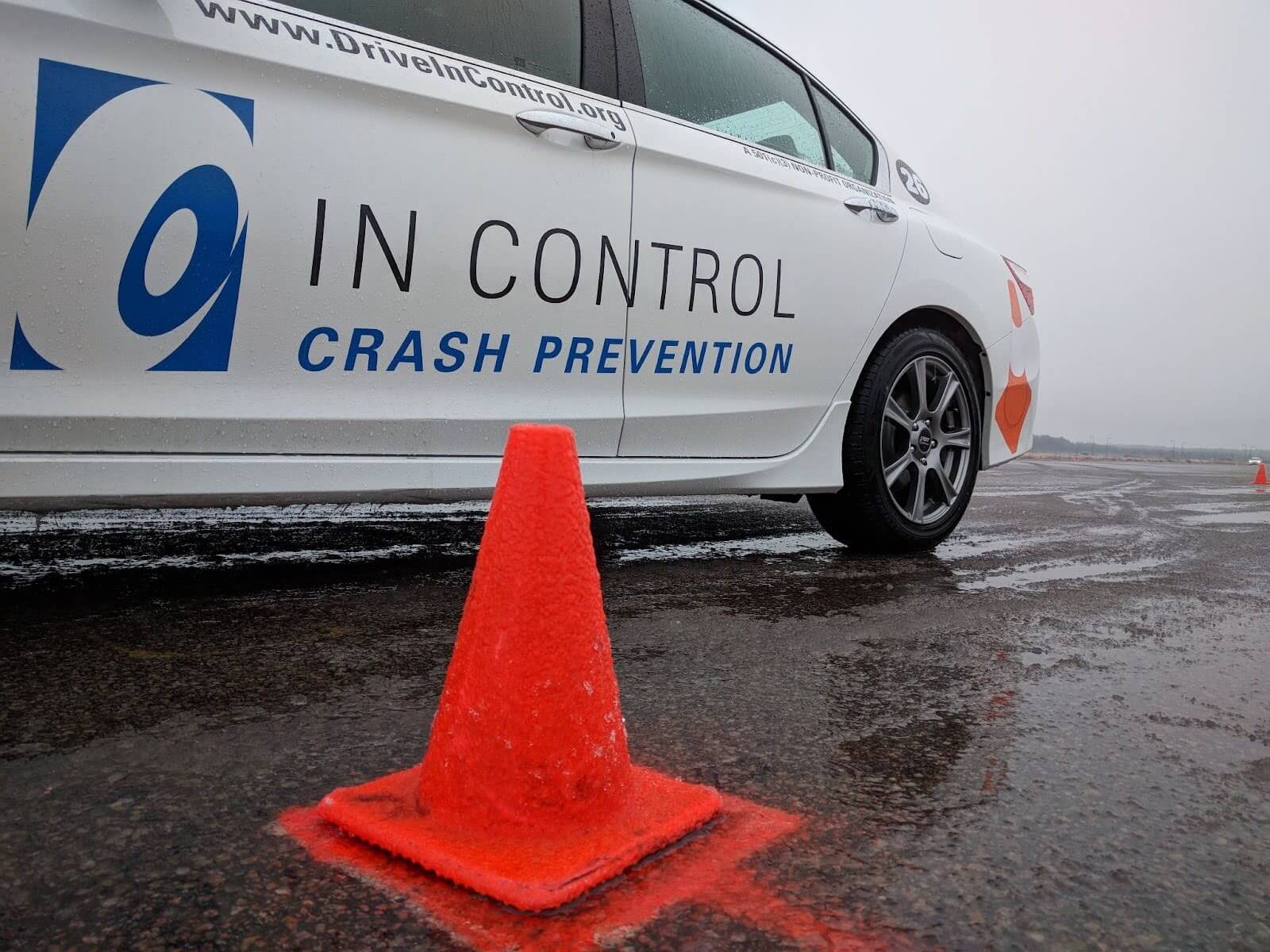 A vehicle driving close to an orange cone in icy, wintery conditions